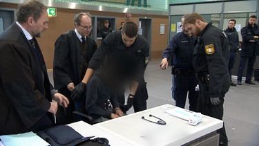 Anwälte und Polizisten stehen um einen der Angeklagten im Gericht in Bamberg. | Bild: BR