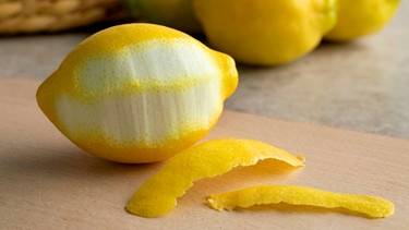Auf einem Tisch liegt eine zum Teil abgeschälte Zitrone; die Schale liegt aufgerollt vor der Zitrone. Im Hintergrund sind zwei Zitronen zu sehen. | Bild: mauritius images / Picture Partners / Alamy
