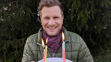 UNSER LAN-Moderator Florian Kienast mit Geburtstagskuchen in den Händen | Bild: BR