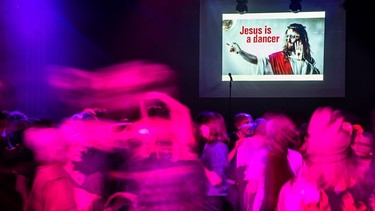 Club-Szene mit vielen Tanzenden. An der Wand ist ein Bild mit der Aufschrift "Jesus is a dancer".  | Bild: Picture Alliance/dpa/Christoph Schmidt
